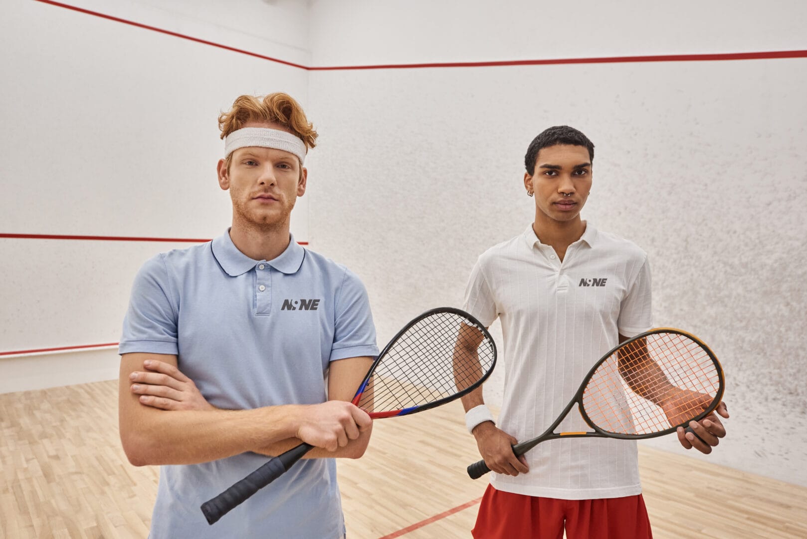Two athletes wearing custom squash apparel and holding rackets on an indoor court.