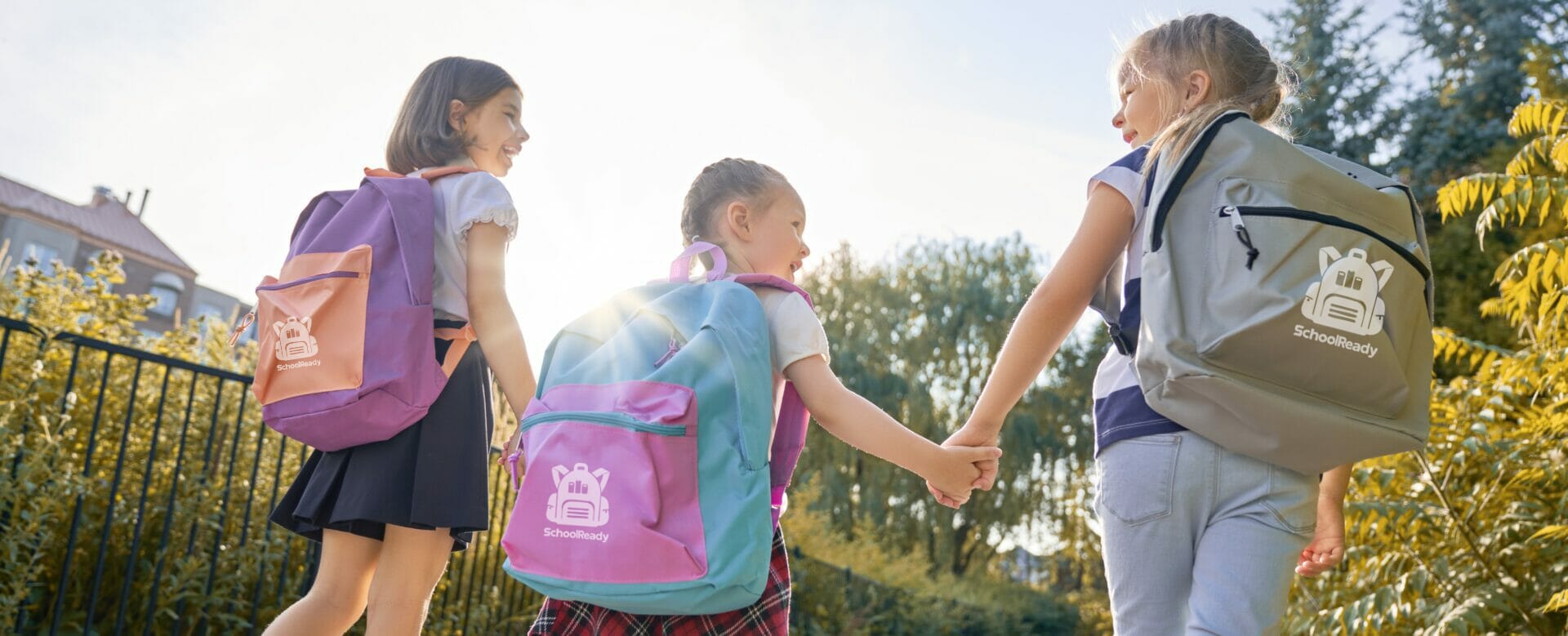 Three children walking outdoors with colorful custom backpacks featuring the “SchoolReady” logo, for branded backpacks