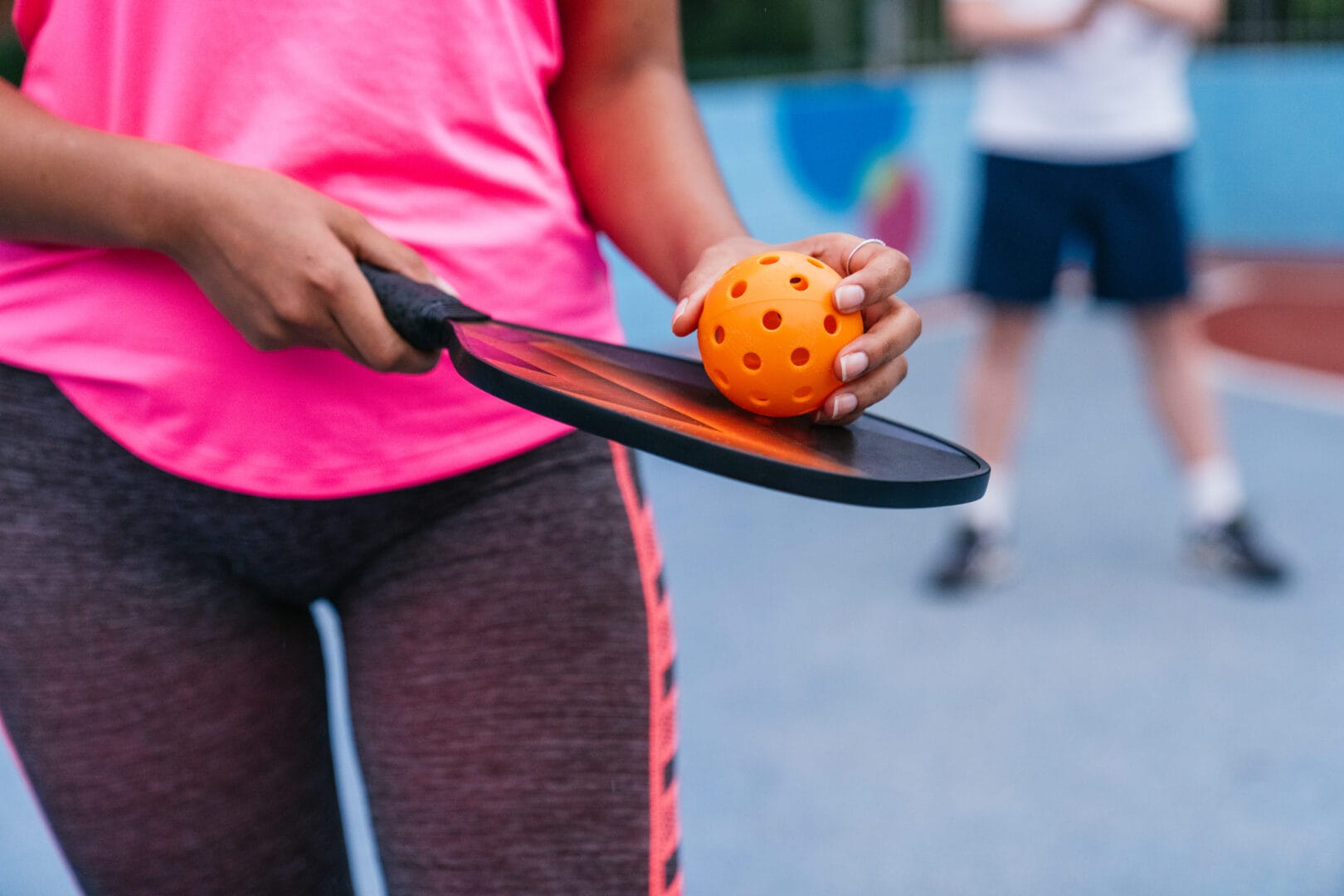 Close up of a woman holding a pickleball paddle and ball, preparing for her serve during a friendly game