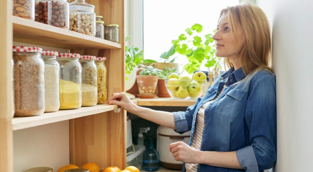 Woman inspecting items on custom retail shelving stocked with jars and fresh fruits in a cozy setup.