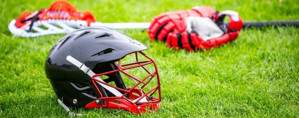 A black helmet and red gloves are shown as part of custom lacrosse gear on green grass.