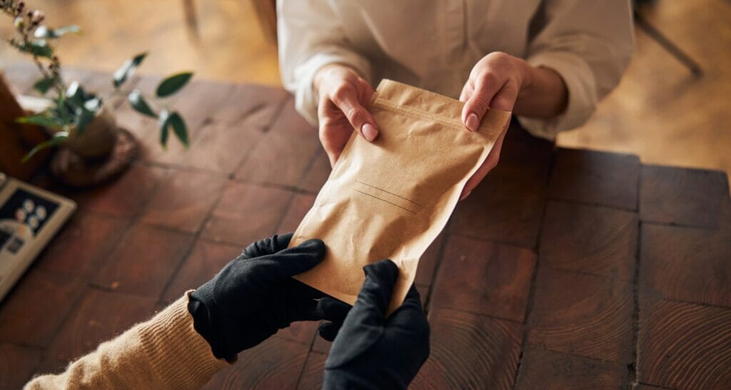 Gloved hands exchange custom packaging pouches in a warm