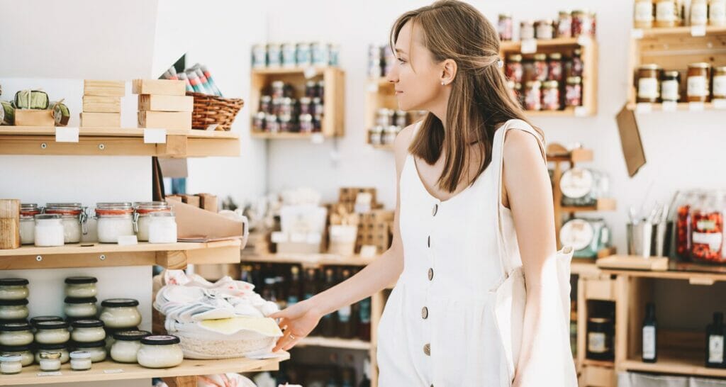 Woman browsing promotional eco friendly products displayed on wooden shelves in a cozy shop.